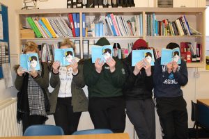 Young people reading a book that covers their faces.