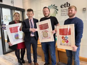 Four people, three holding framed posters. 