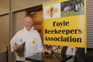 Image of beekeeper beside a Foyle Beekeepers Associaion banner.