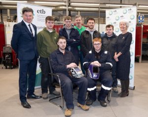 Image of welding competitors sitting down with judge and managers. standing up 