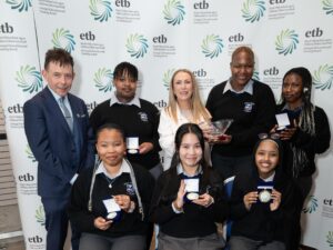 Group of students and staff seated and standing holding medals and a bowl.